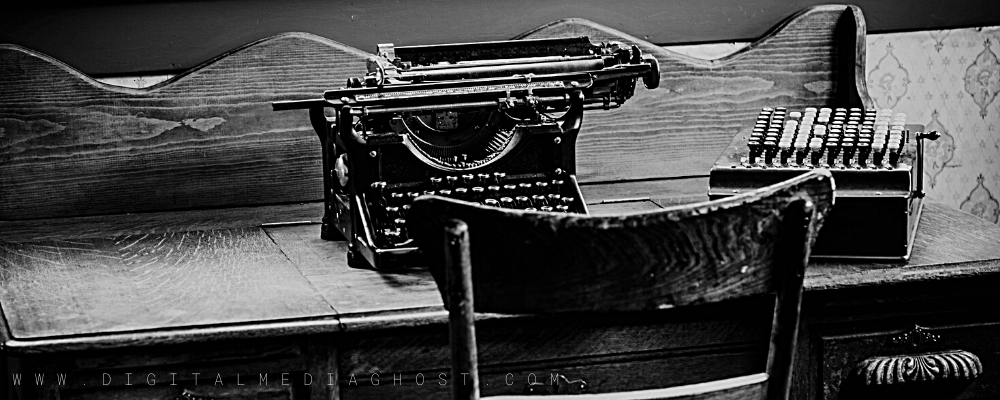 Black and white image of a vintage typewriter on an antique desk with chair by a window.